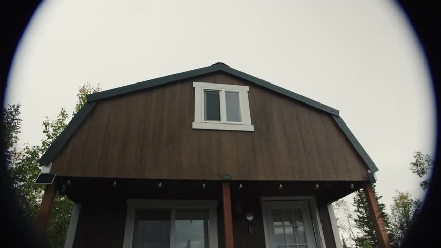 Facade of a small wooden house with white windows under a cloudy sky