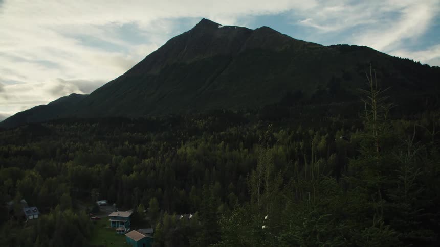 Mountain surrounded by vegetation with a few houses to the side outdoors during day time