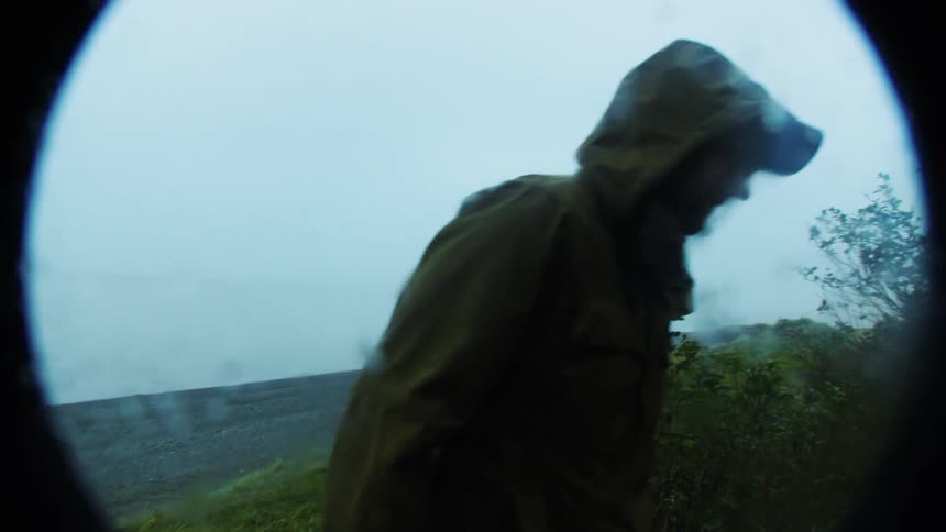 Person walks through a foggy rainy landscape surrounded by rough vegetation