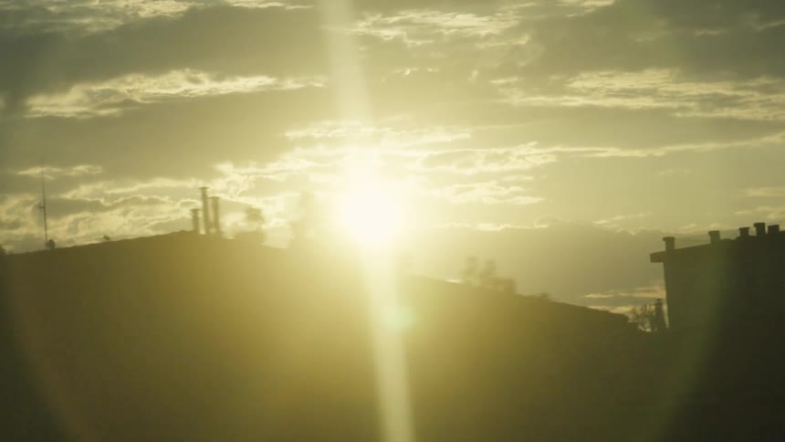 Sun sets behind dark rooftops under a cloudy sky