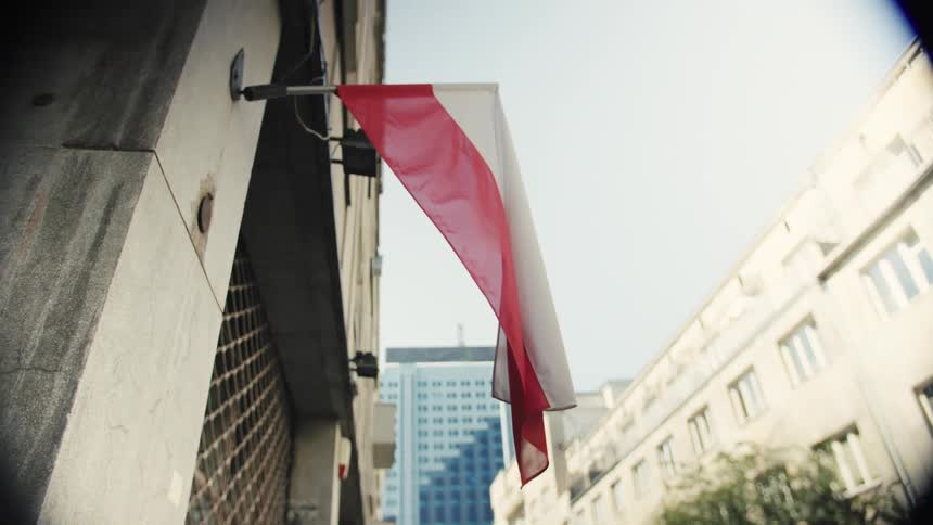 Close up of a red and white flag handing outdoors from a building in a metropolitan city during daytime