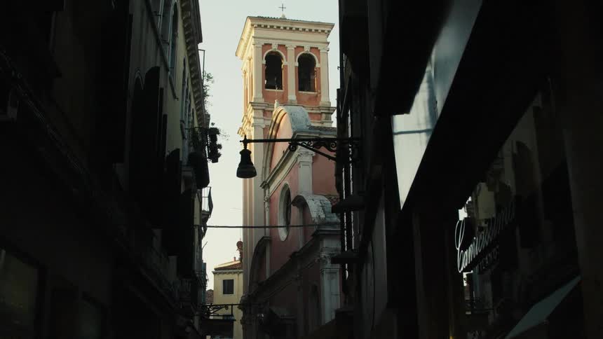 Historic church tower rises between narrow buildings at sunset