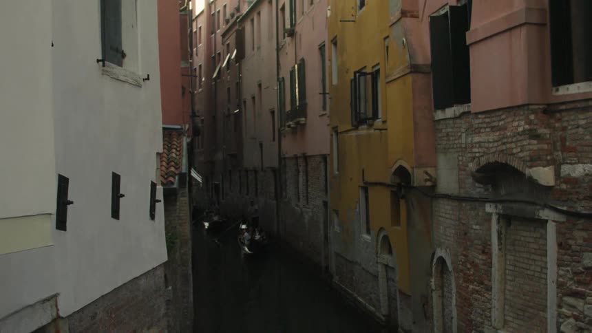 A gondola glides through a narrow shadowed canal between timeworn brick buildings the water catching small flashes of light