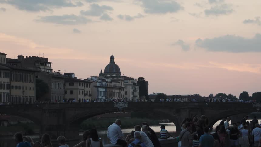 The video features a scenic view of a historic european city along a river at dusk or sunrise a domed building stands prominently on the far bank visible over a crowded stone bridge crossing the water