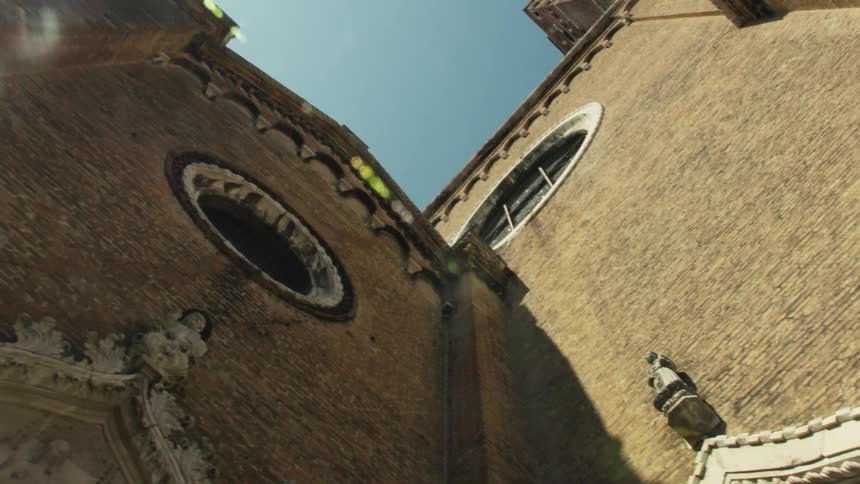 The video is an extreme lowangle shot that pans up a tall narrow brick facade of an old european church focusing on its ornate gothicstyle entrancethe camera movement reveals the weathered brickwork and upward into the bright clear sky with a