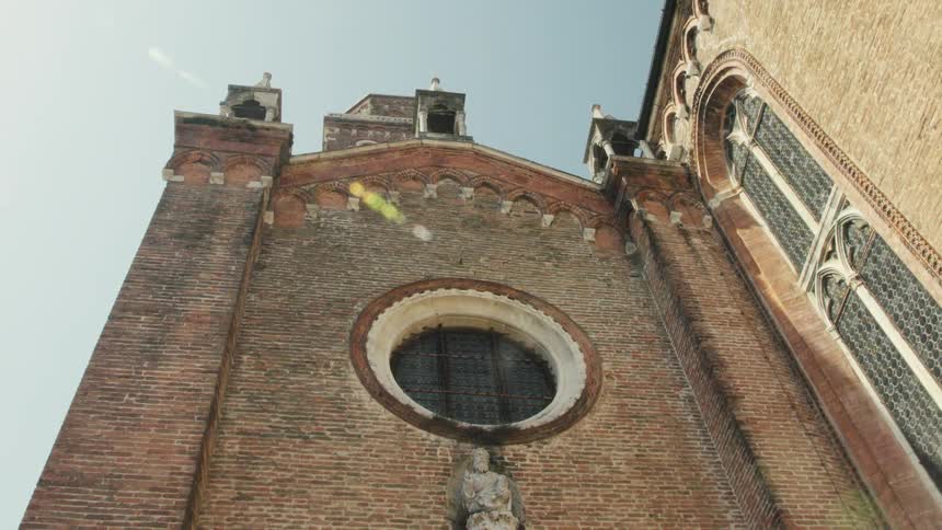 Facade of a brick church seen from below with a circular window and a sculpture above the entrance
