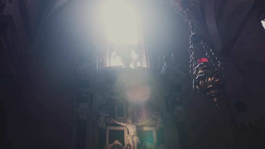 The video captures a dimly lit interior of a church or cathedral focusing on a crucifixion scene or altar a strong beam of natural light shines down from a high window or opening creating a dramatic ethereal atmosphere