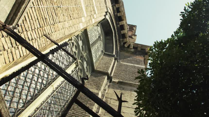 Historic brick building with vertical columns and arched decorated windows partially obscured by tree