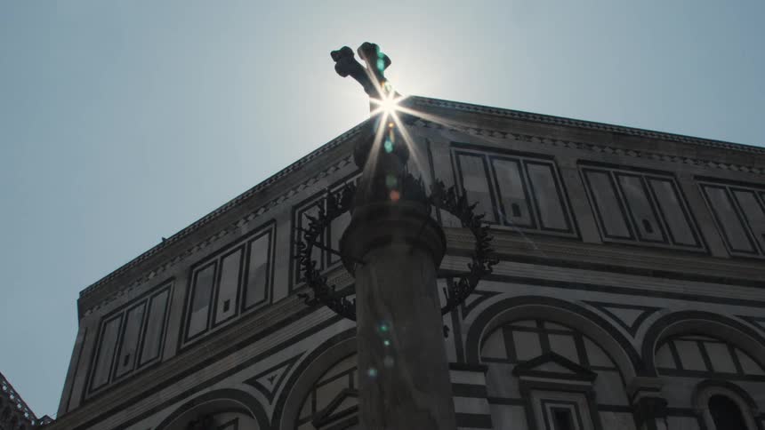 A tower with a cross symbol standing in front of a large building outdoors during daytime