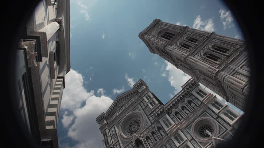 The video is an extreme lowangle wideshot possibly a fisheye effect that captures the intricately designed facade of the florence cathedral duomo and its towering campanile bell tower the medieval structures fill the frame against a