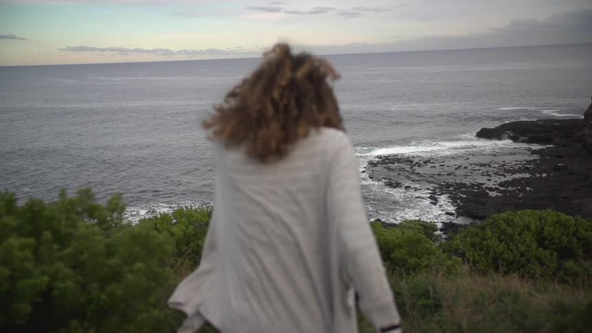 Woman walking down a hill towards an ocean