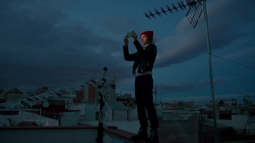 Woman in a red beret photographs the evening sky from a rooftop