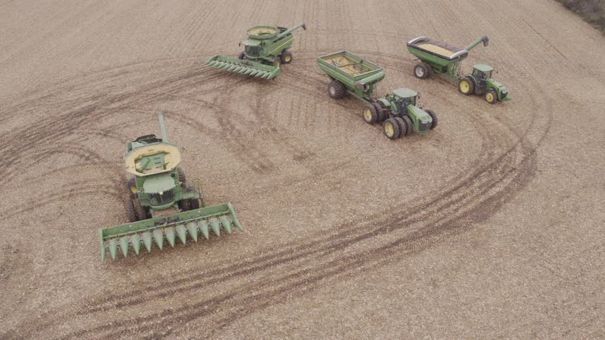 Agricultural machines lined up in a harvested field with circular tire tracks on the ground