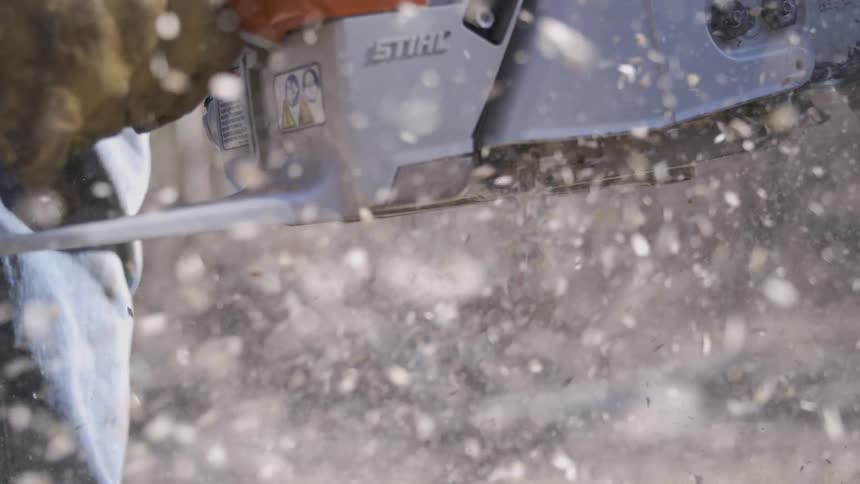 Close up of a male logger cutting a tree log with a chainsaw outdoors during daytime