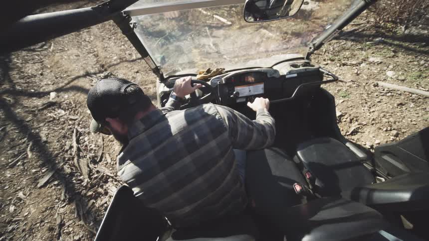 Man wearing a cap and plaid shirt reversing a vehicle on a dirt terrain