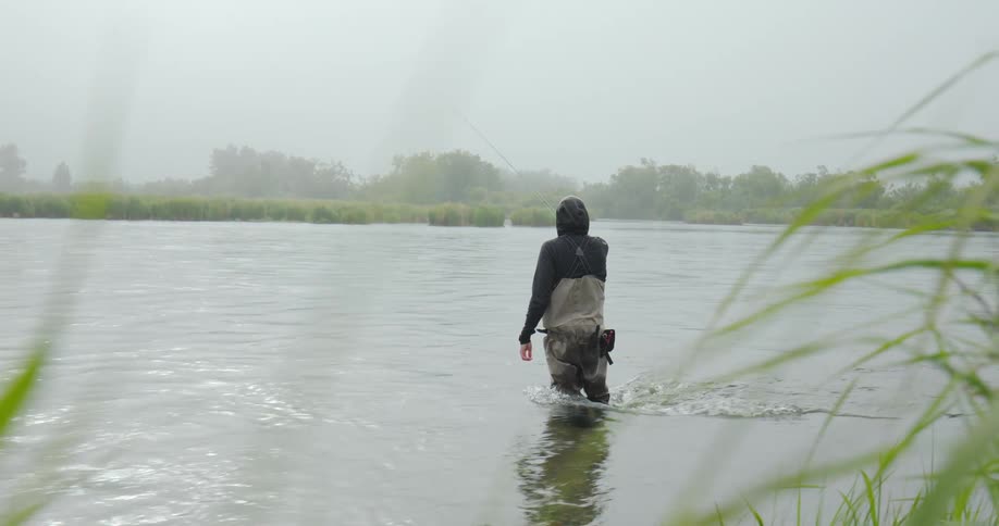 Angler in waterproof gear fly fishing in a river under cloudy weather