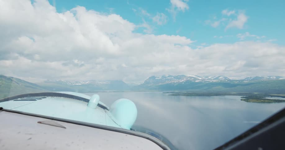 A scenic flight from a planes cockpit perspective reveals a vast lake and snow capped mountains under a cloudy sky