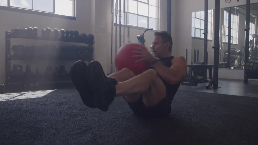 A middleaged man works out in the gym at midday using an exercise ball to strengthen his core and improve balance under the bright overhead lights