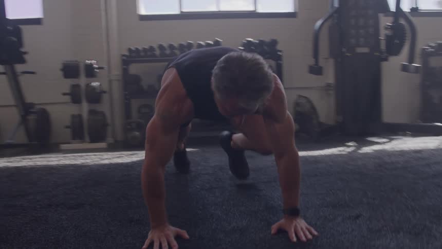 A middle aged man exercising on the floor in a gym during daytime