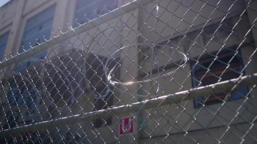 Metal fence with barbed wire in front of a building under bright sunlight