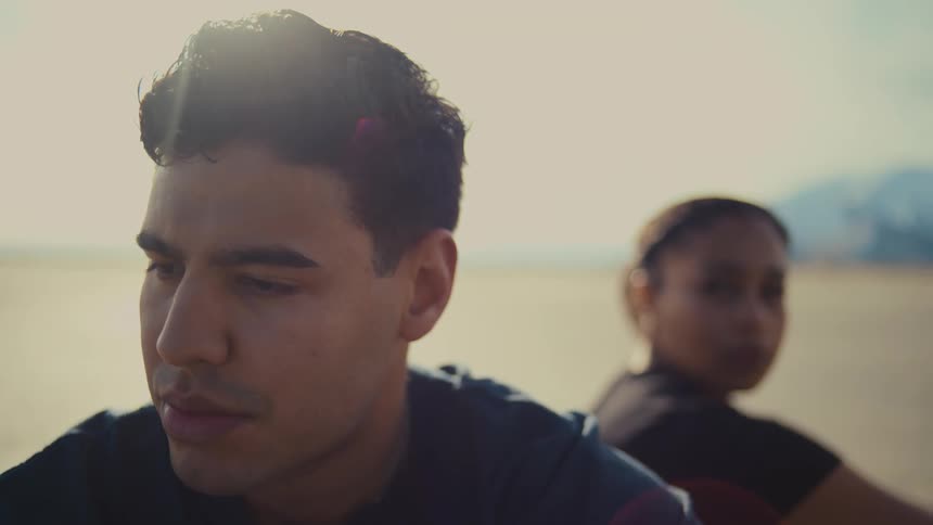 A couple sits apart and lost in thought amid a sunlit landscape