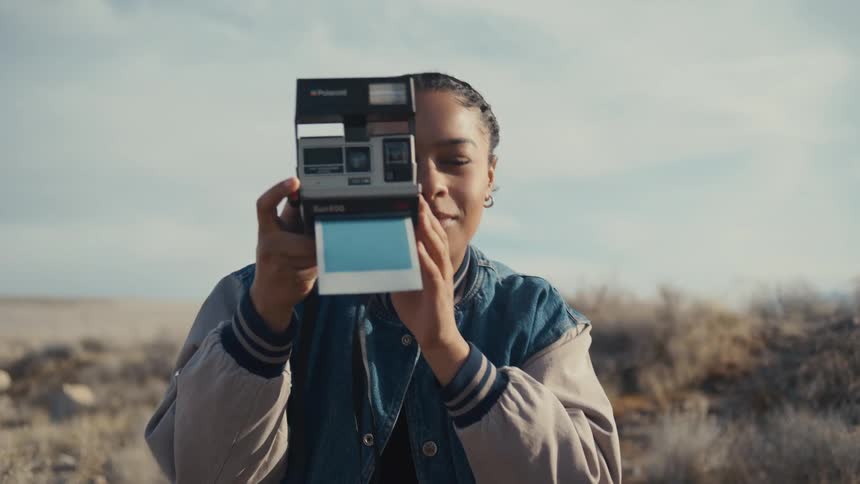 A woman takes a picture with an instant camera and looks at it afterwards