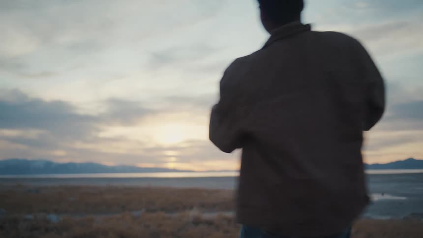 Couple spins joyfully holding hands in dry grass with mountains behind