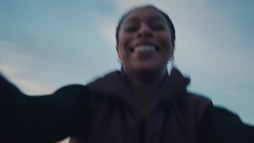 A woman smiles at the camera while recording herself outdoors at dusk