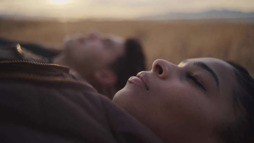 Two people lie in a field at sunset gazing quietly toward the sky