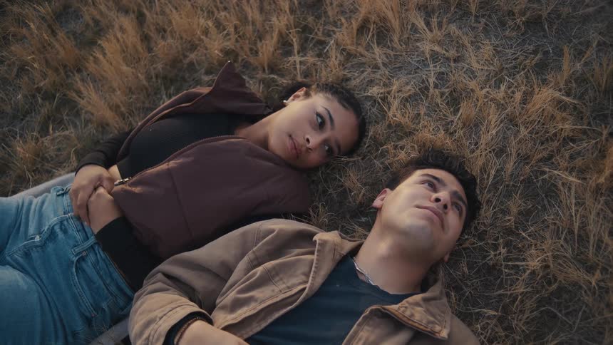 A couple lay on brown grass the male gazes up at the sky as the female looks at him