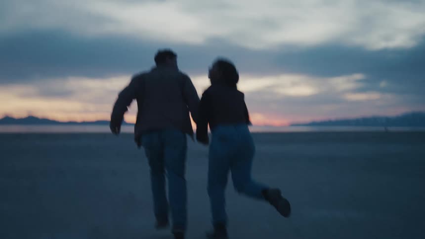 Silhouetted couple runs hand in hand across arid landscape at sunset