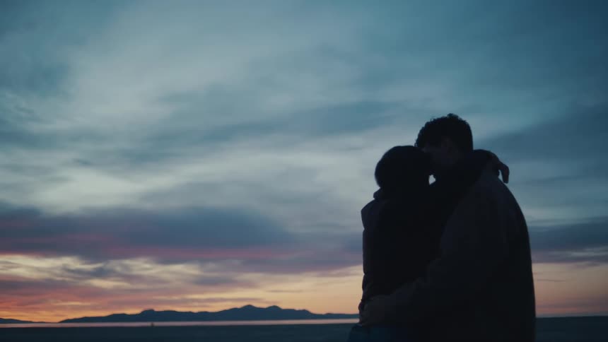 Couple shares an intimate moment against sunset with mountains behind