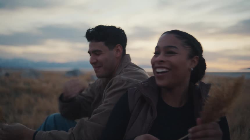 Young man and young woman laughing and playfully poking each other with a plant outdoors during dusk or dawn