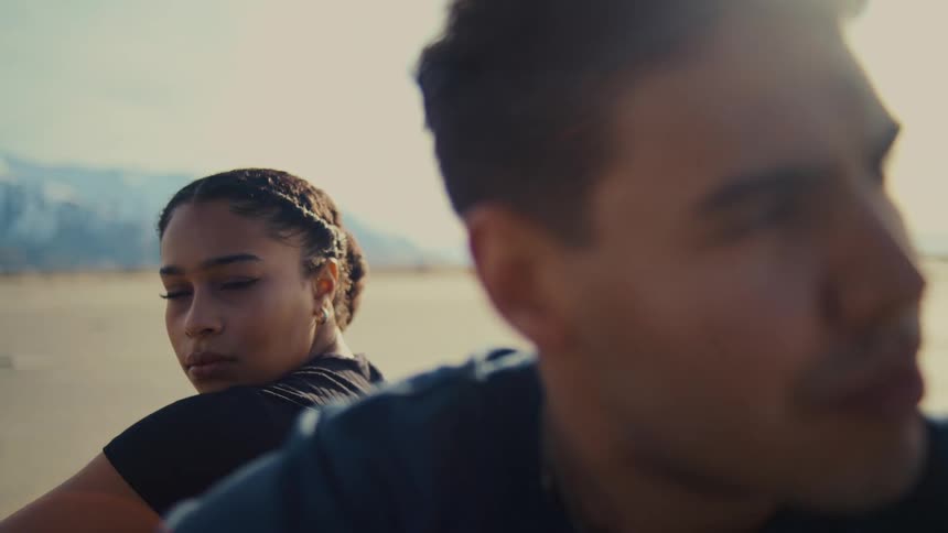 Young man and young woman sitting with their backs at each other frowning and contemplative outdoors during day time