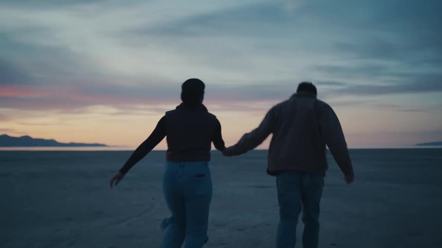 Couple runs hand in hand across a wide open landscape at sunset