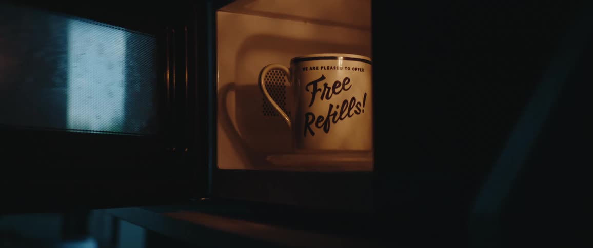 Tattooed hand placing a mug with the phrase free refills inside a lit microwave
