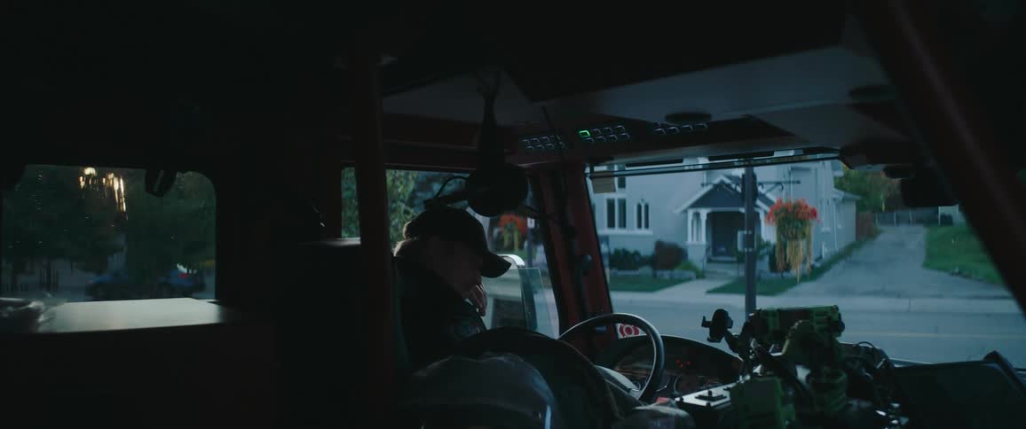 Firefighter sitting at the wheel of a truck parked on a residential street at dawn