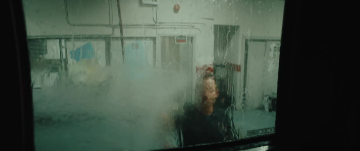 The video shows a man from the waist up viewed from the side energetically scrubbing what appears to be a truck or ambulance window with a highpressure hose or scrubber seen through the constantly running sheet of water on the glassthe man who