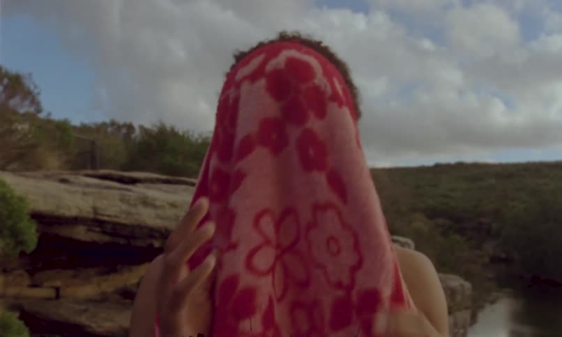 Person drying their face with a pink towel near a natural landscape