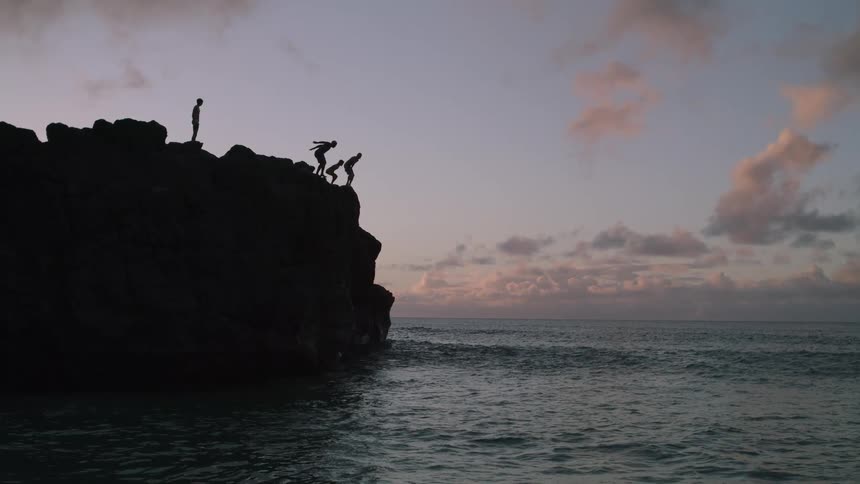 The video clip is a silhouette of a cliff jumping scene against a dark sky several people are visible standing on the edge of the dark cliff preparing to jump into the ocean below