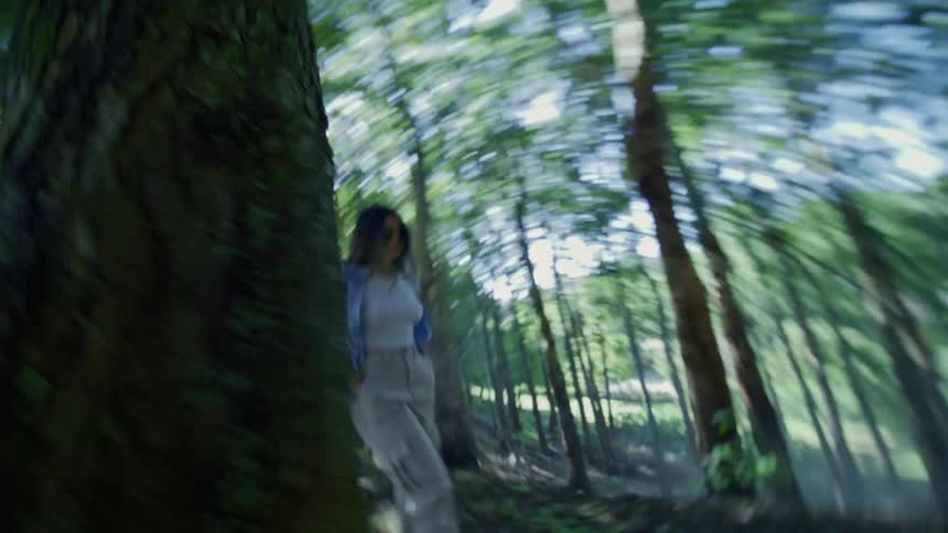 A woman in a lightblue top and cargo pants walks through a sunlit forest captured with a swirling motion