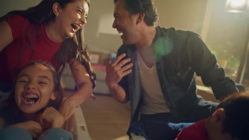 A joyful family of four has a playful moment laughing together their children in plastic storage bins