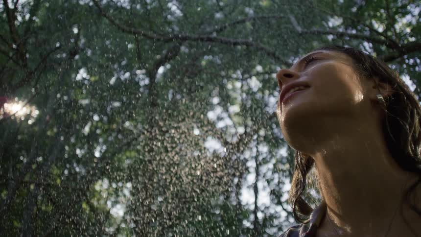 Woman looking up as water droplets fall through the trees
