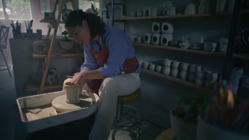 A young woman moulding pottery on a wheel indoors in a pottery room
