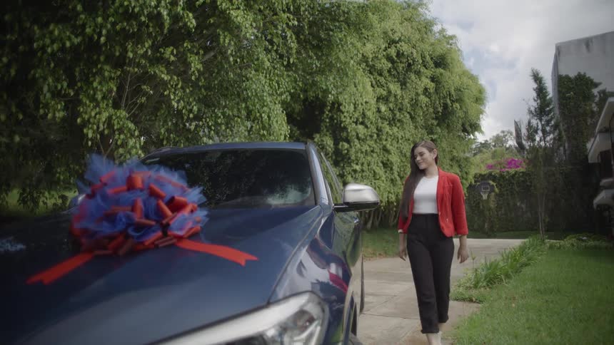 A young woman admiring her car gift parked outdoors during daytime