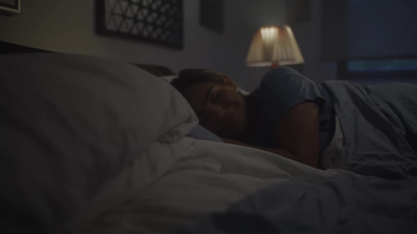 Woman lying in bed smiling softly under the light of a bedside lamp