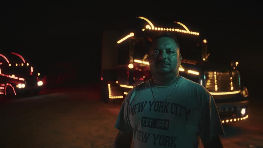 A middle aged hispanic man standing in front of parked cargo trailers outdoors at night