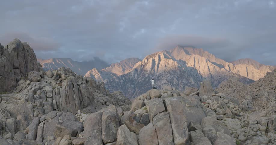 Man standing on top of a rocky elevation on a mountainous region outdoors during dusk or dawn