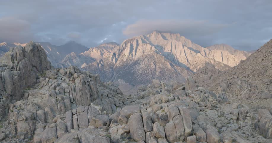 Male hiker stands on a rock formation and looks at the mountainous scenery on a cloudy day
