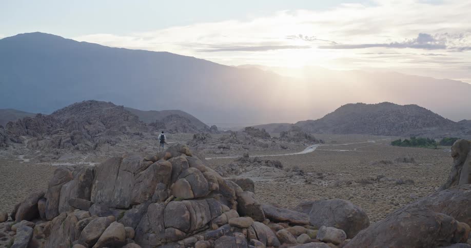 A man stands on a cliff in the wilderness watching the sunset after a long hike as golden light spills across the horizon
